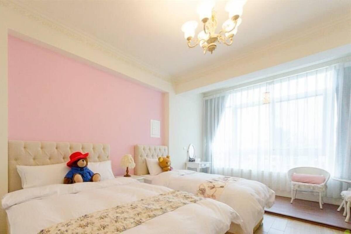 Un dormitorio con dos camas, una lámpara de araña, una ventana con cortinas y una silla.