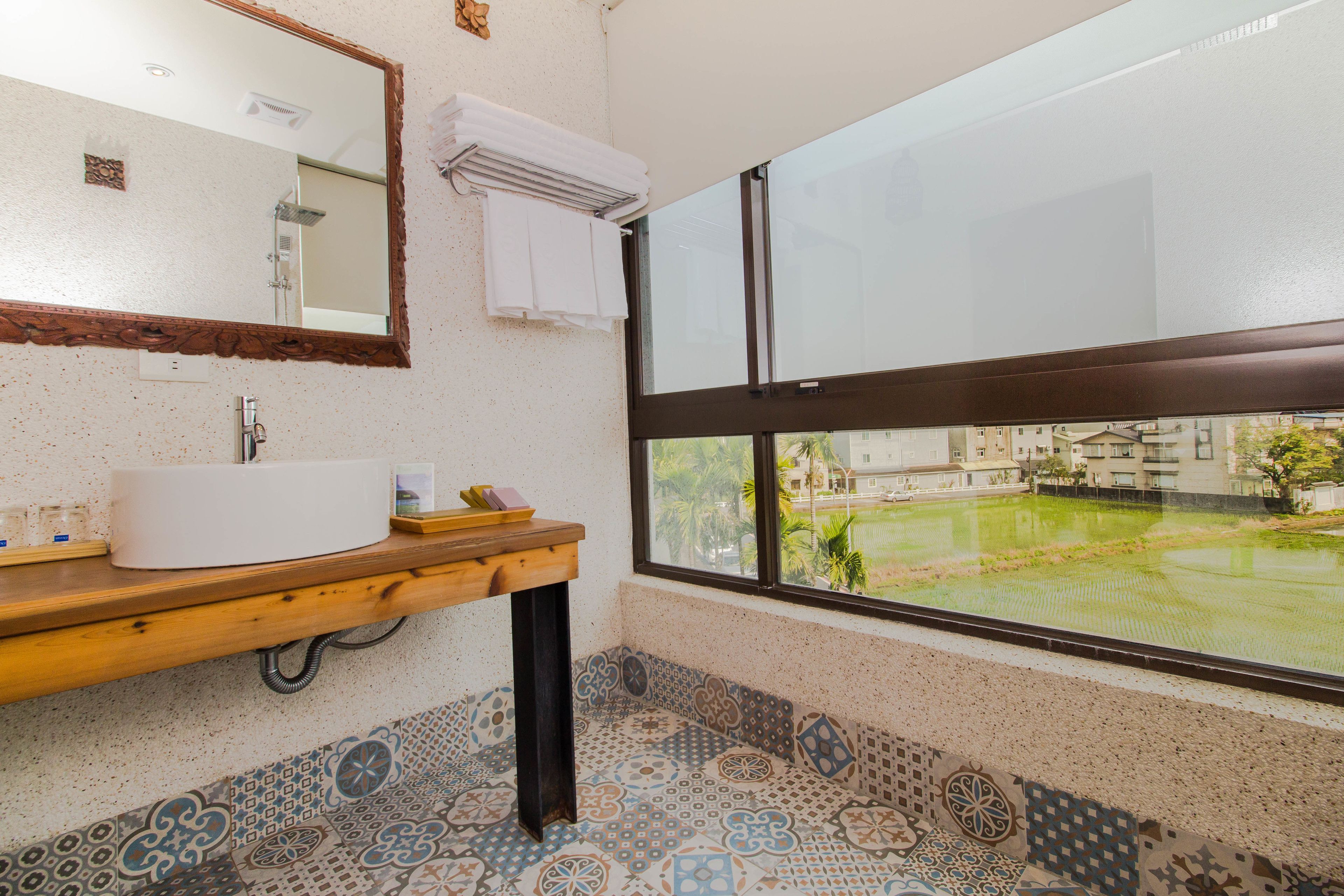 A bathroom with a large mirror, a sink, and a window with a view of buildings and greenery.