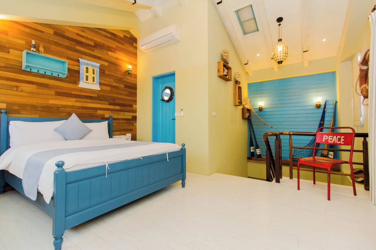 A bedroom with a blue bed, a red chair labeled "PEACE," and a wooden wall with built-in shelves.