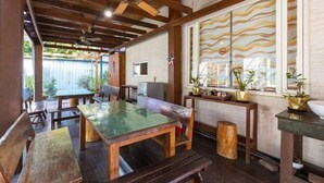A covered outdoor dining area with wooden tables and benches, a ceiling fan, and a view of the outdoors through large windows. - Yi Shin Garden Hostel (Shoufeng)