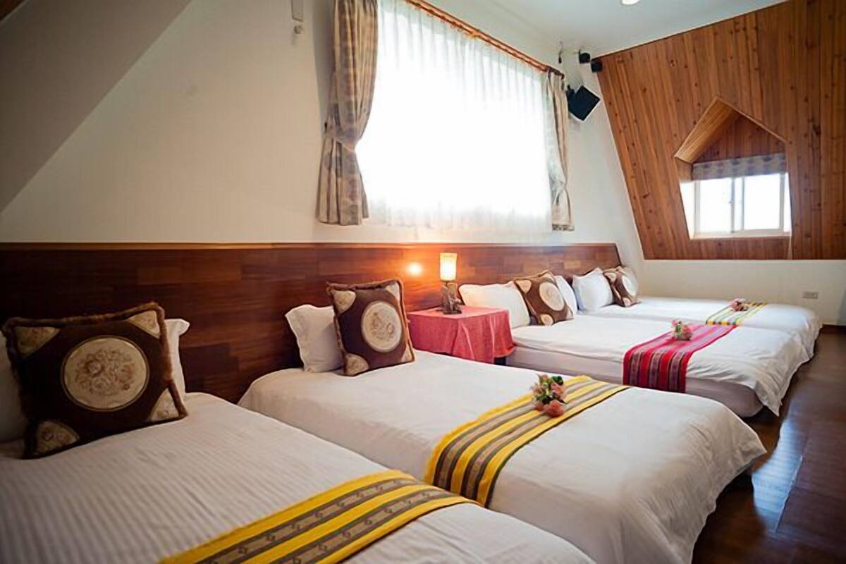 A hotel room with three beds, a wooden ceiling, and a large window with curtains.