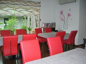 A dining area with red chairs and tables, a bookshelf with books, and a wall with floral decorations. - Yi Shin Garden Hostel (Shoufeng)