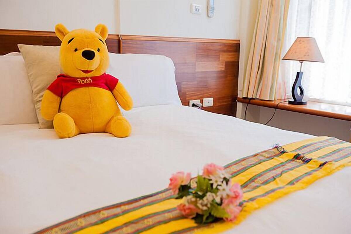 A bed with a plush toy, a bedside lamp, and a floral arrangement.