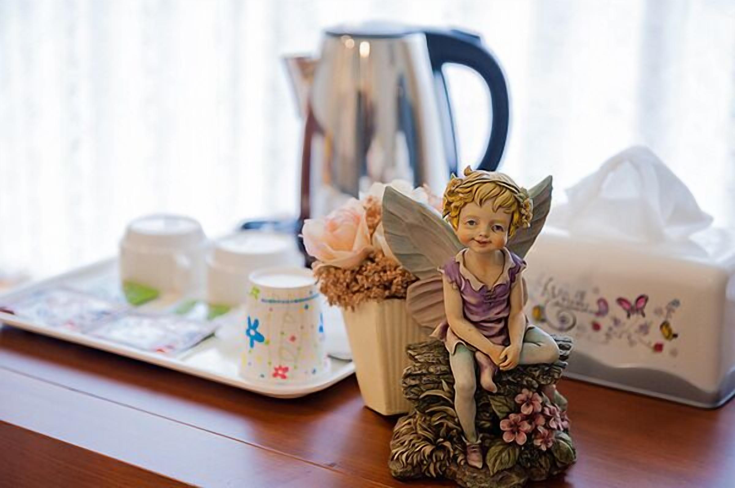 A table with a fairy figurine, a coffee cup, a teapot, and a decorative box.