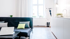 A modern living room with a dark blue sofa, a laptop on a side table, and a view of a window with curtains. - Boom Apartments (Kraków)
