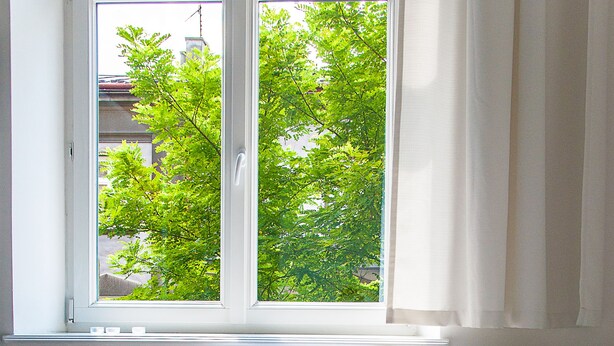 A neatly made bed with a window view of trees, a bedside table with a laptop, and a knitted blanket on the bed. - Boom Apartments (Kraków)