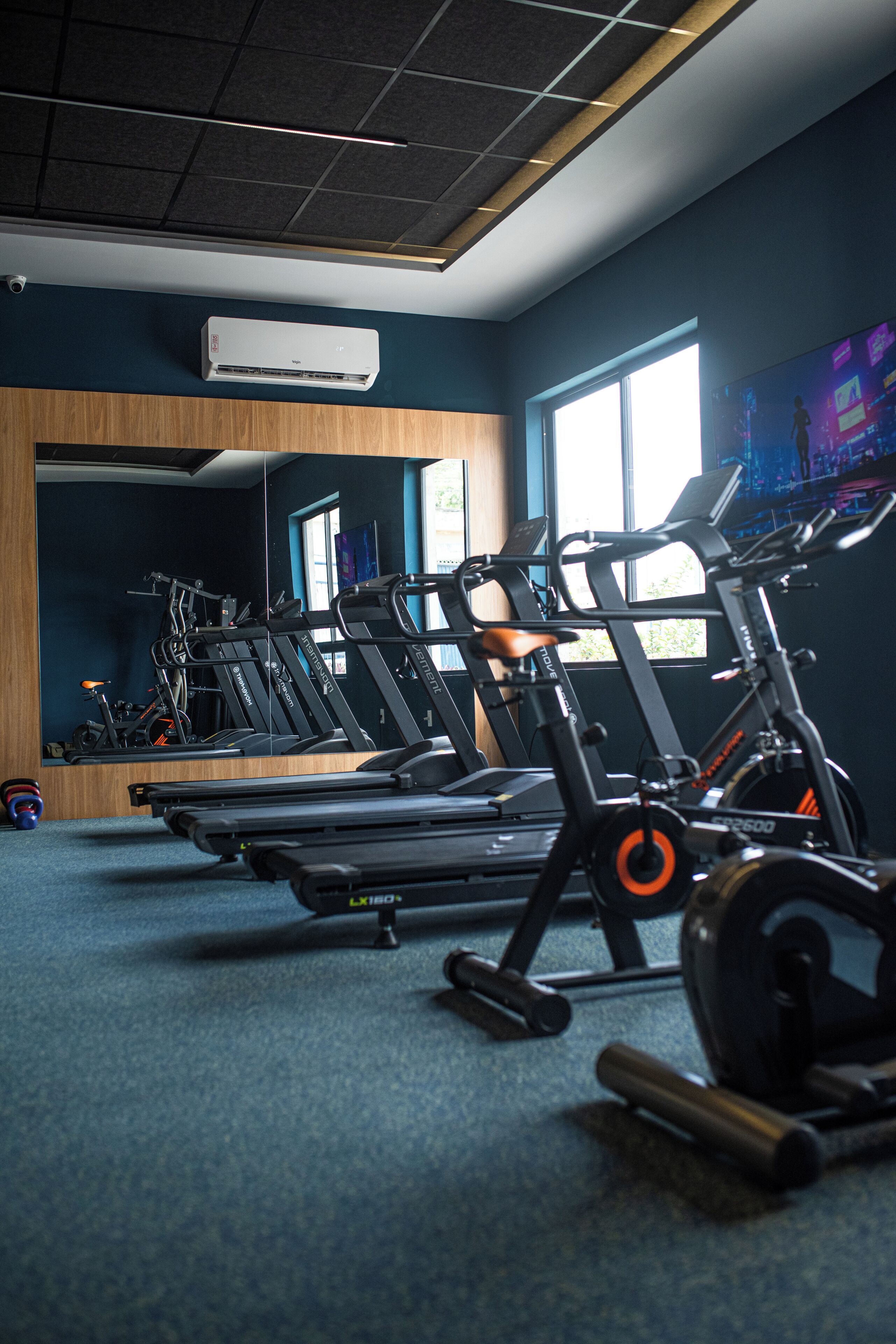 Un gimnasio con cintas de correr, bicicletas estáticas y un espejo grande.