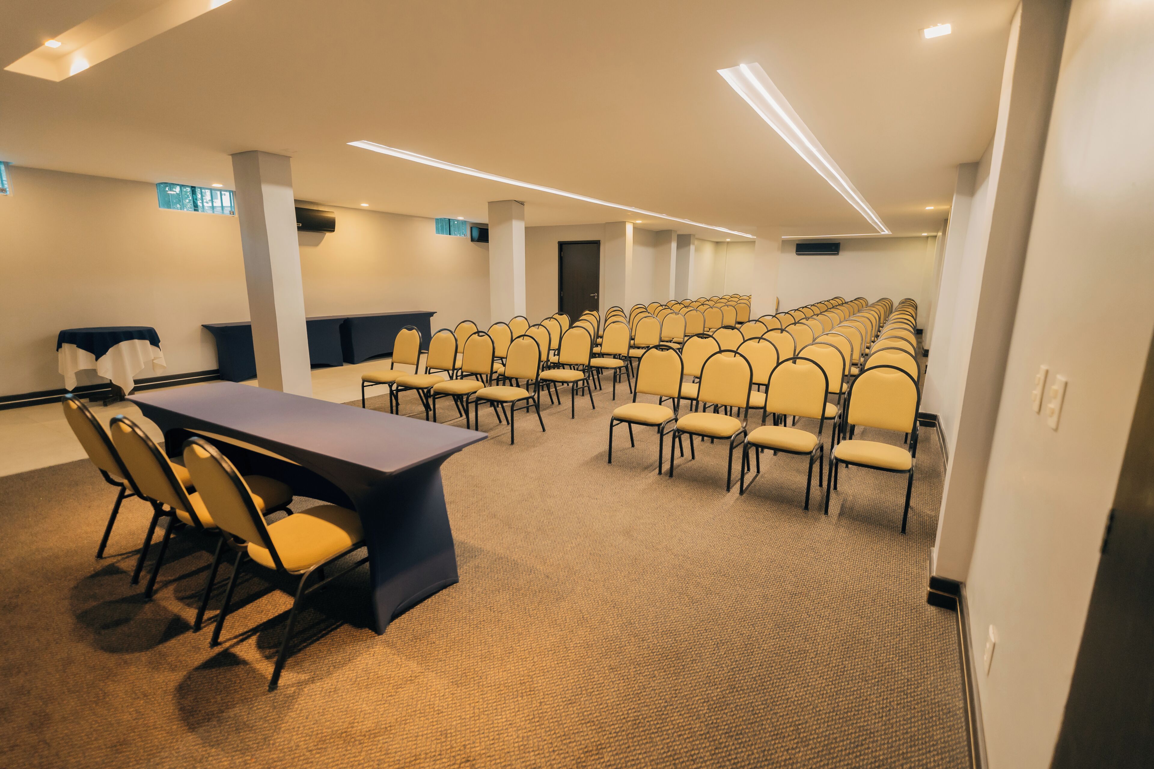 Un salón de conferencias con una larga mesa, varias sillas y piso alfombrado.