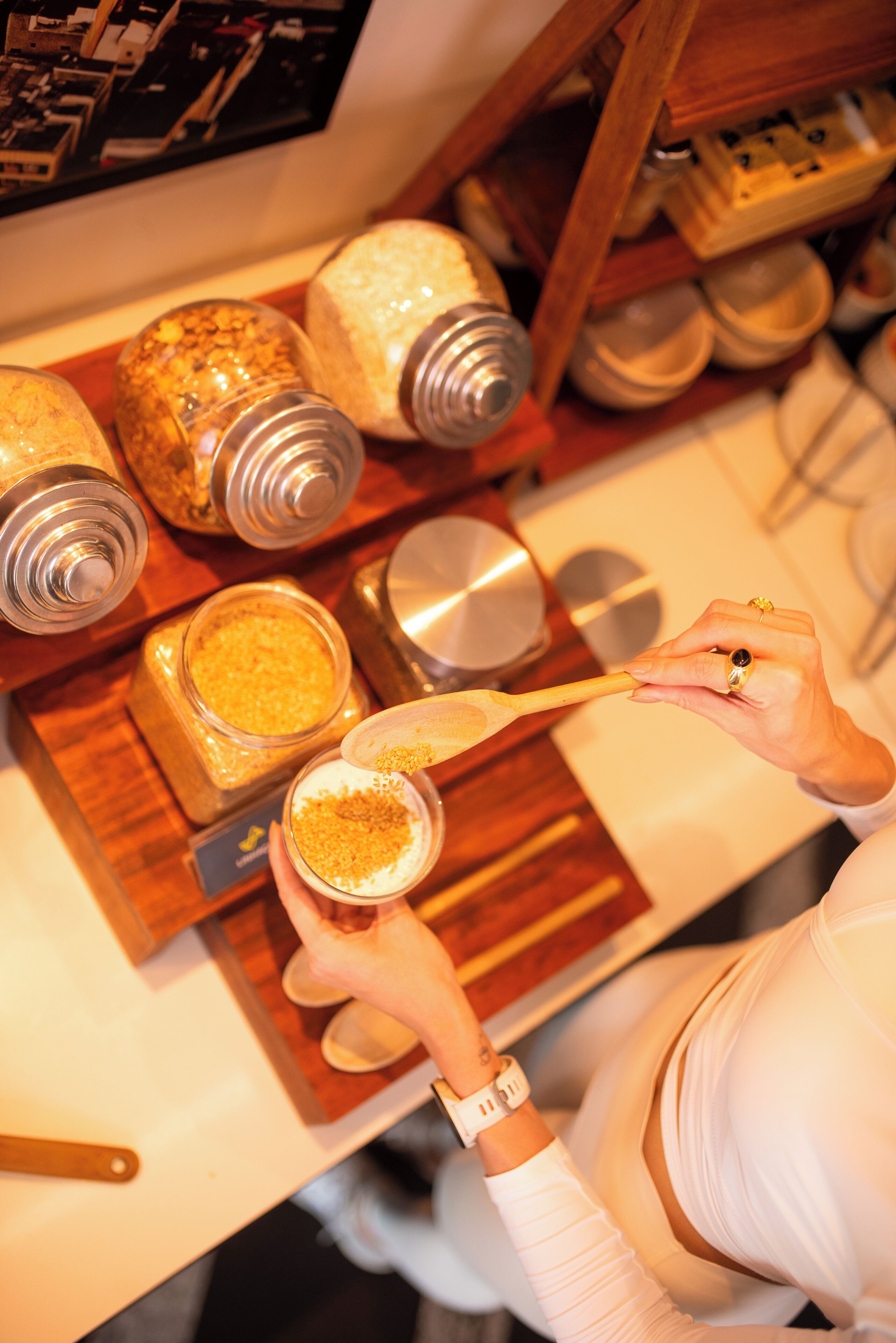 Una persona sosteniendo una cuchara con un producto granuloso, rodeada de frascos y recipientes sobre una tabla de madera.