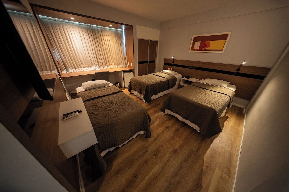 A hotel room with two beds, a desk, a chair, a window with curtains, and a painting on the wall.