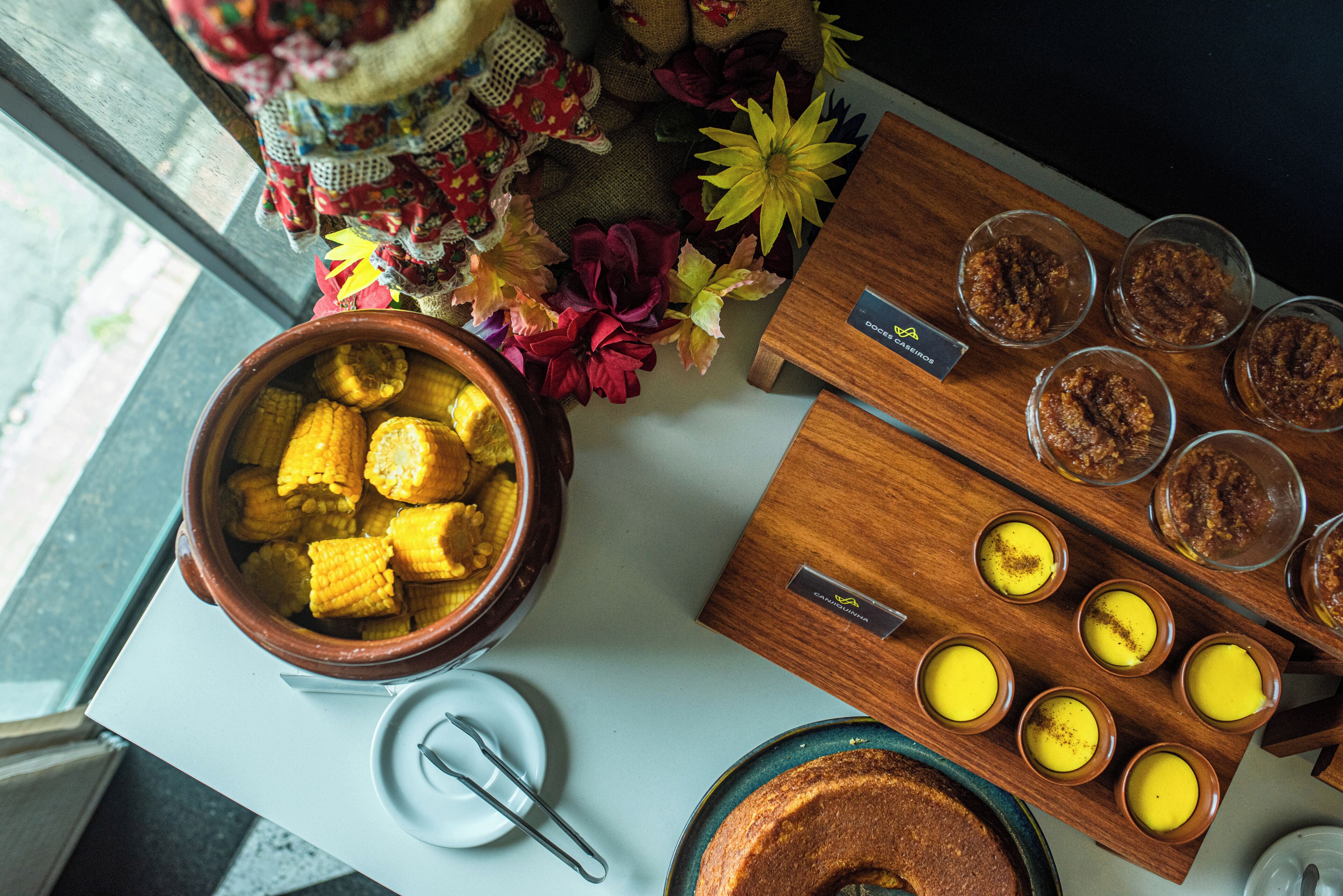Een tafel met een kom maïs, een taart en verschillende kleine schaaltjes met gele, custardachtige desserts.