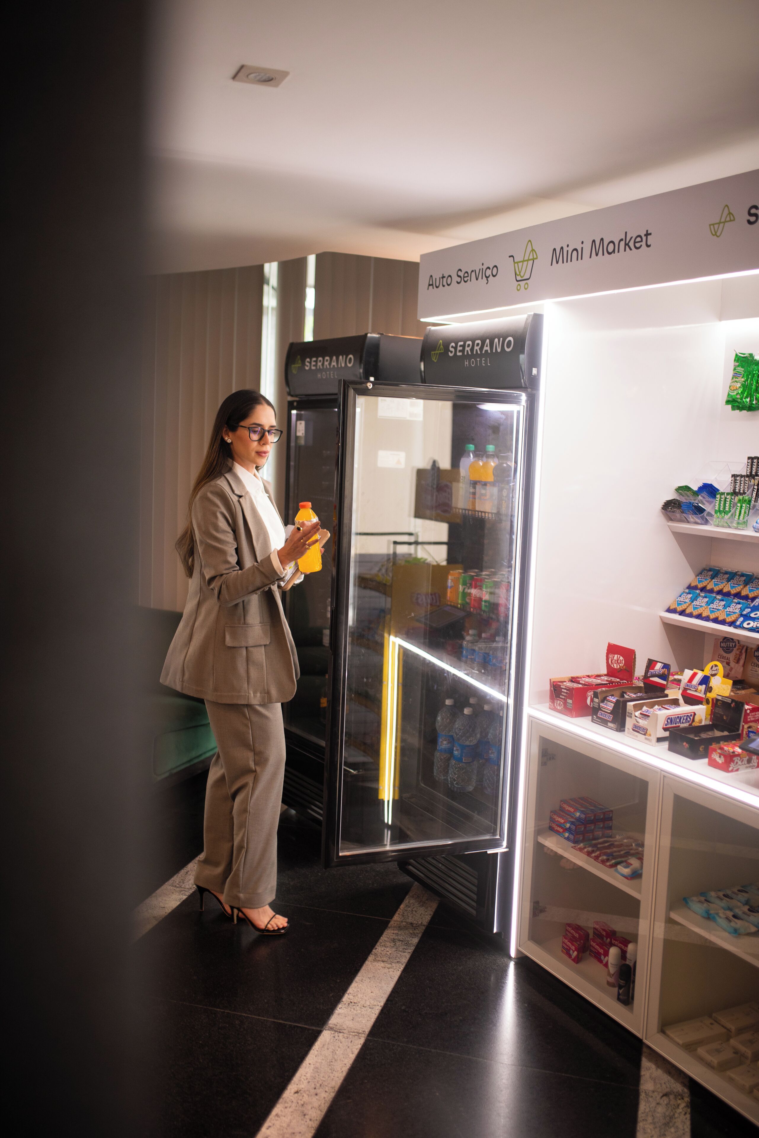 A person in a business suit standing next to a refrigerator with a mini market sign above it.
