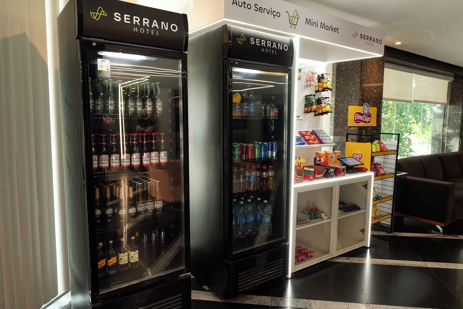 Two beverage dispensers in a hotel lobby with a mini market and seating area.