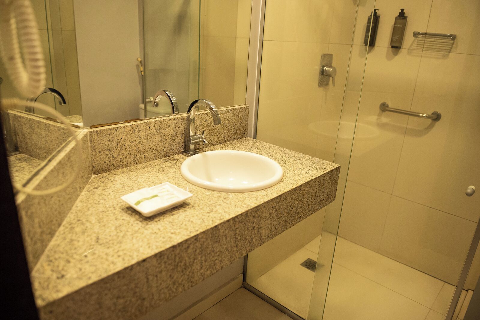 Un baño con encimera de granito, lavabo blanco, espejo, cabina de ducha de vidrio y toallero.