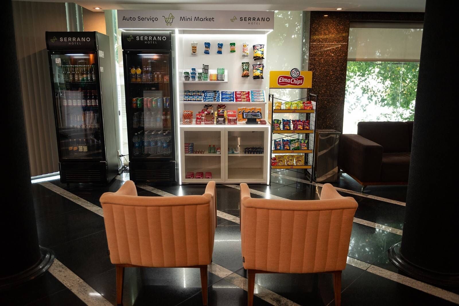 Een hotel lobby met een kleine winkel, automaten en een zithoek.