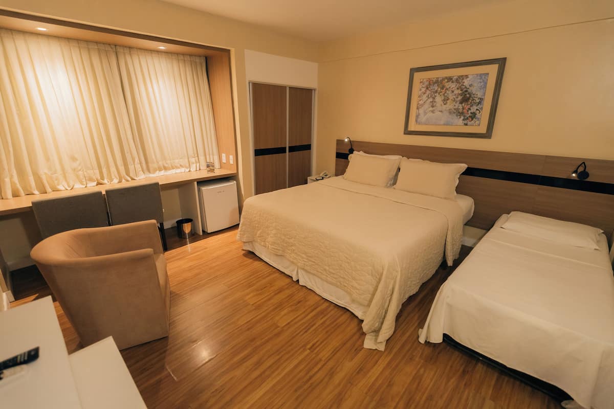 A hotel room with a large bed, a desk with a chair, a wardrobe, and a painting on the wall.