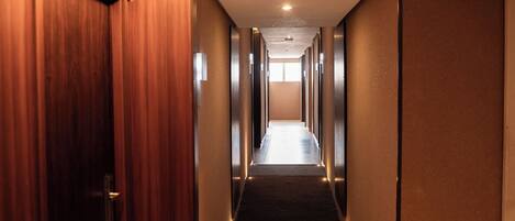 A hotel hallway with wooden doors on one side and a carpeted floor.