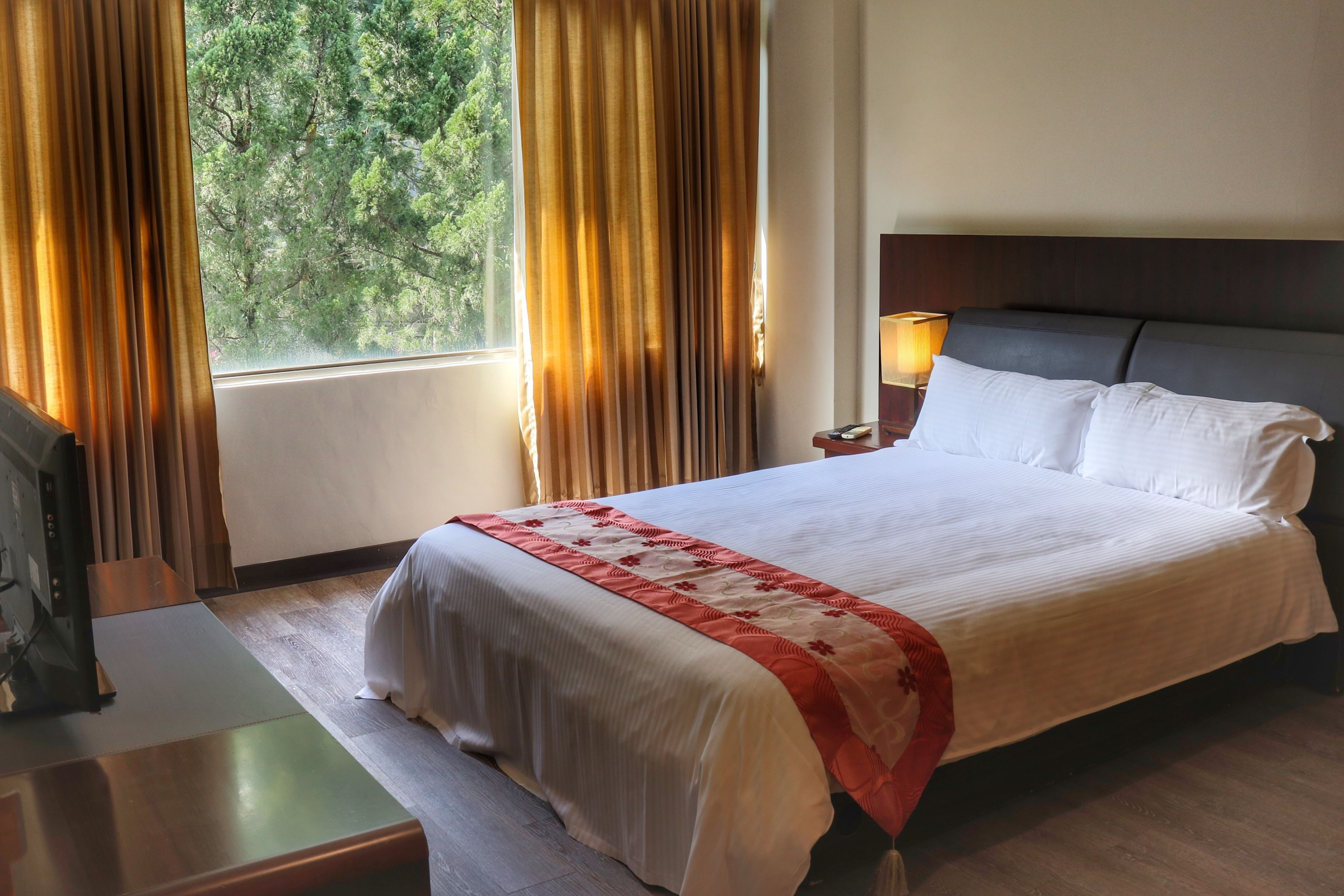 A hotel room with a bed, a desk, a lamp, and curtains.