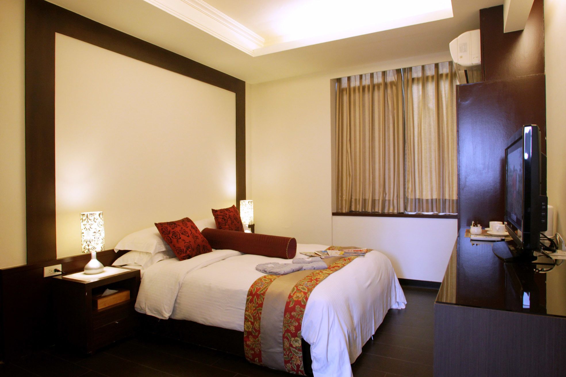 A hotel room with a large bed, two bedside tables with lamps, a television, and a window with curtains.