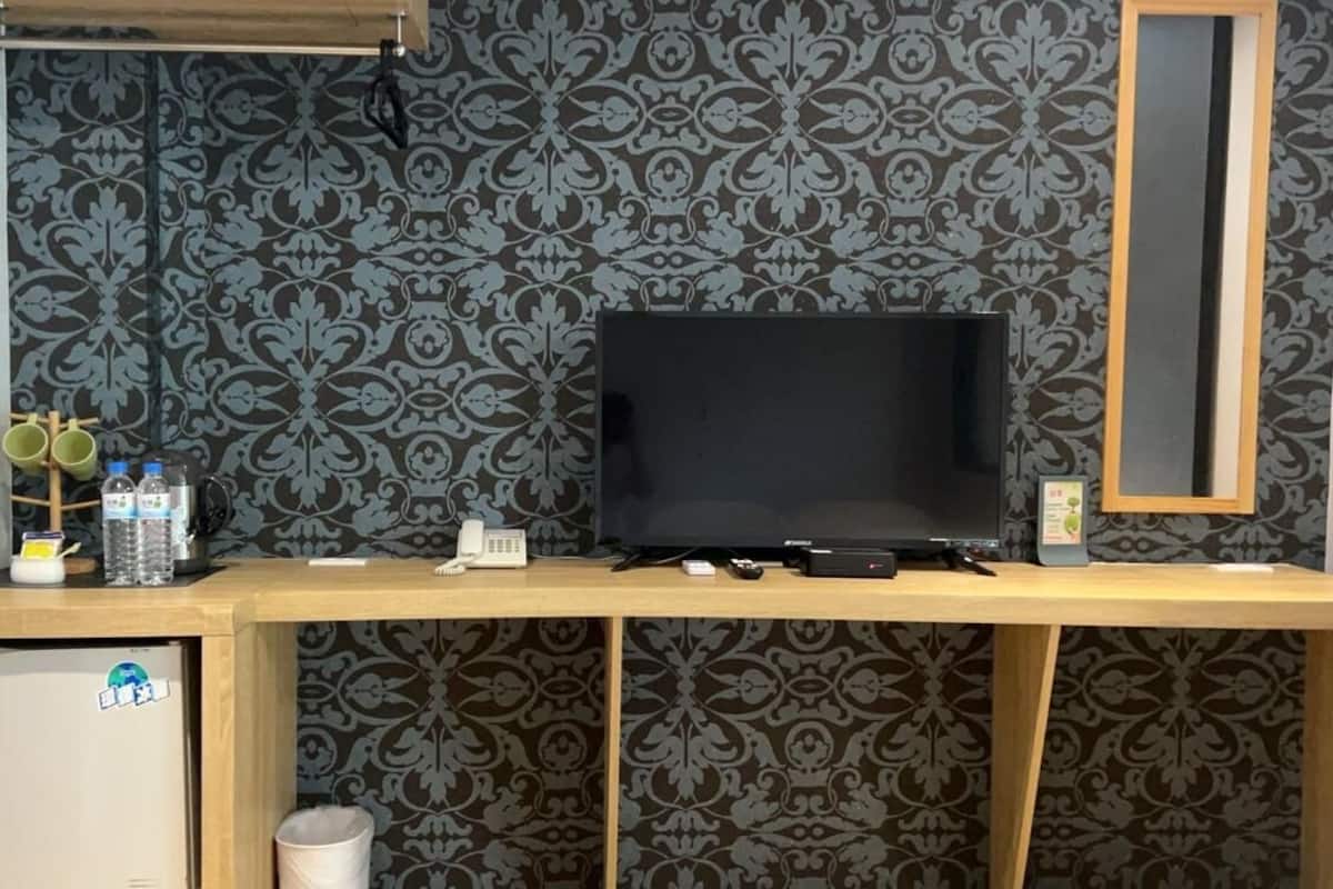 A wooden desk with a flat-screen TV, a small fridge, and a trash can.