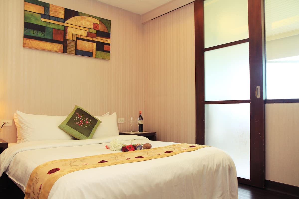 A hotel room with a bed, a nightstand, a painting, and a window.