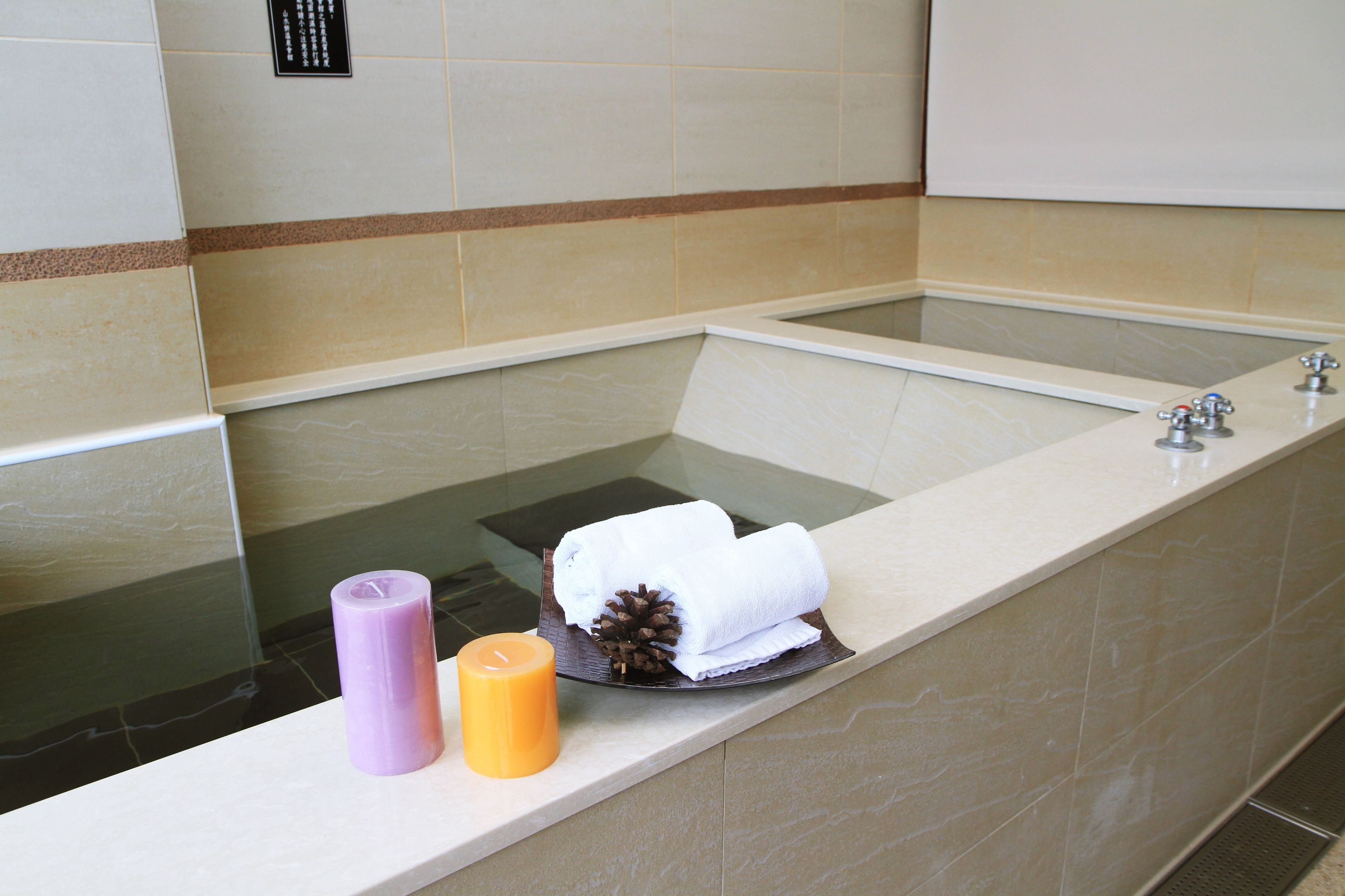 Uma banheira com toalha e decoração de pinha, uma vela roxa e uma vela amarela na borda.