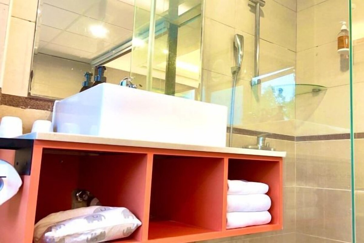 A bathroom with a white sink, a glass shower enclosure, and a red storage shelf with towels.