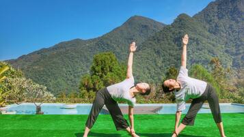 Two people performing yoga on a green lawn with a mountain backdrop.