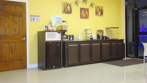 Zona de recepción con puerta de madera, señalización de baño, mostrador con máquina de café y decoración en la pared.