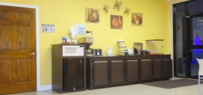A reception area with a wooden door, a counter with a microwave, a coffee machine, and wall art.