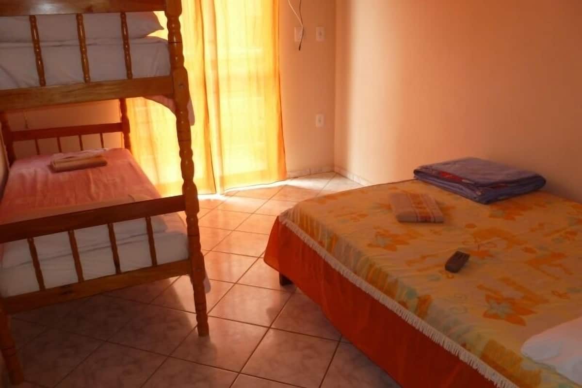 A room with a bunk bed, a single bed, and a window with curtains.