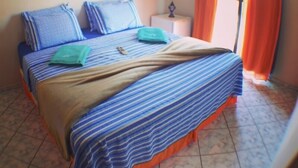 Una cama con ropa de cama a rayas, una mesita de noche con una lámpara y cortinas naranjas.