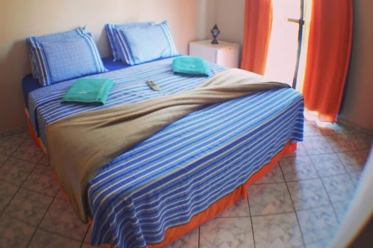 A bed with striped bedding, a bedside table with a lamp, and orange curtains.
