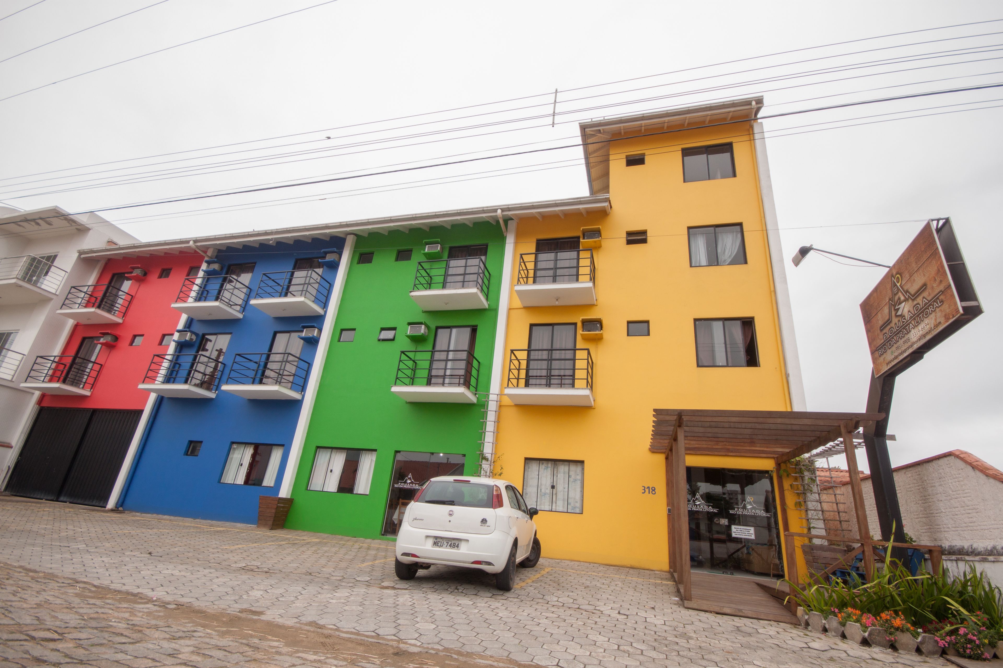 A multi-story building with colorful facades in red, blue, green, and yellow. A white car is parked in front.