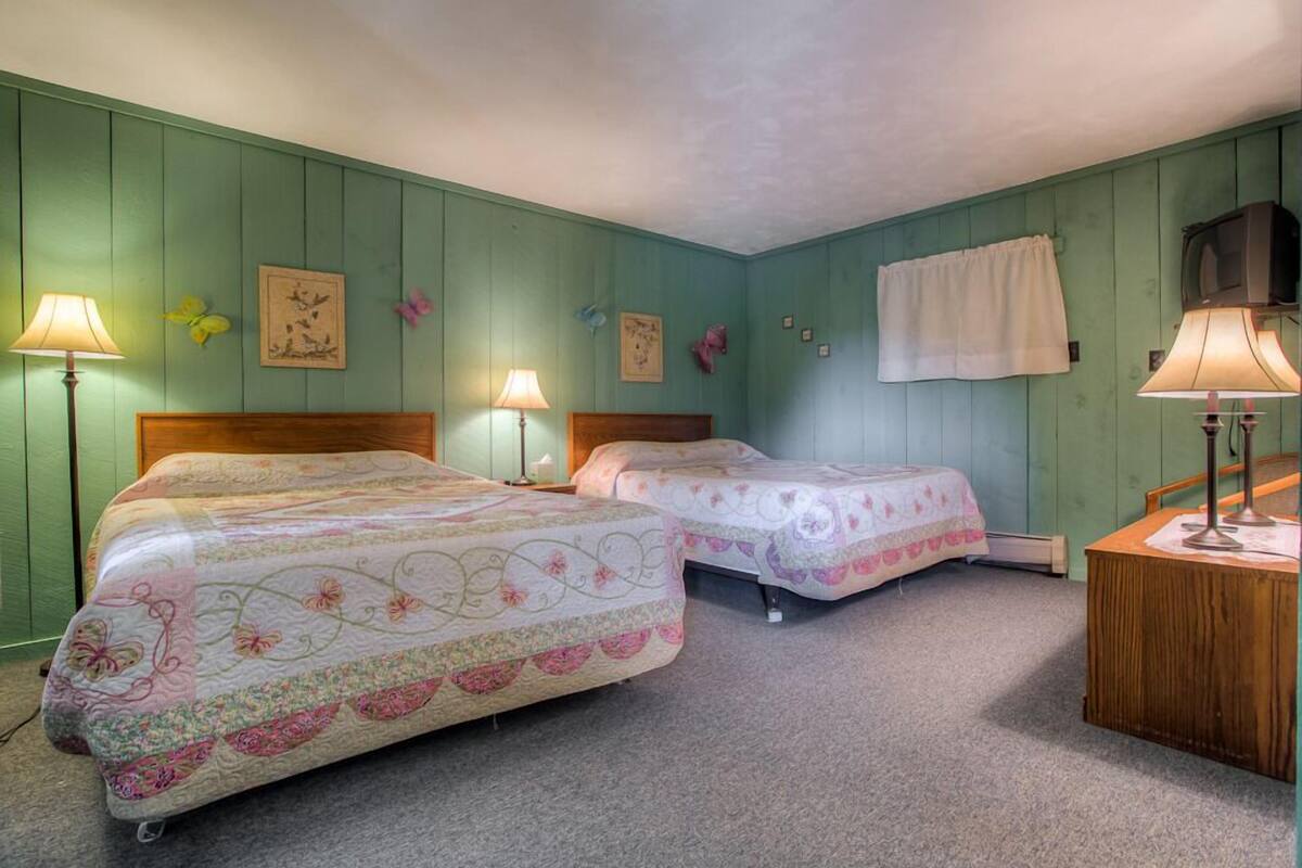 A room with two beds, a wooden nightstand, and a television.