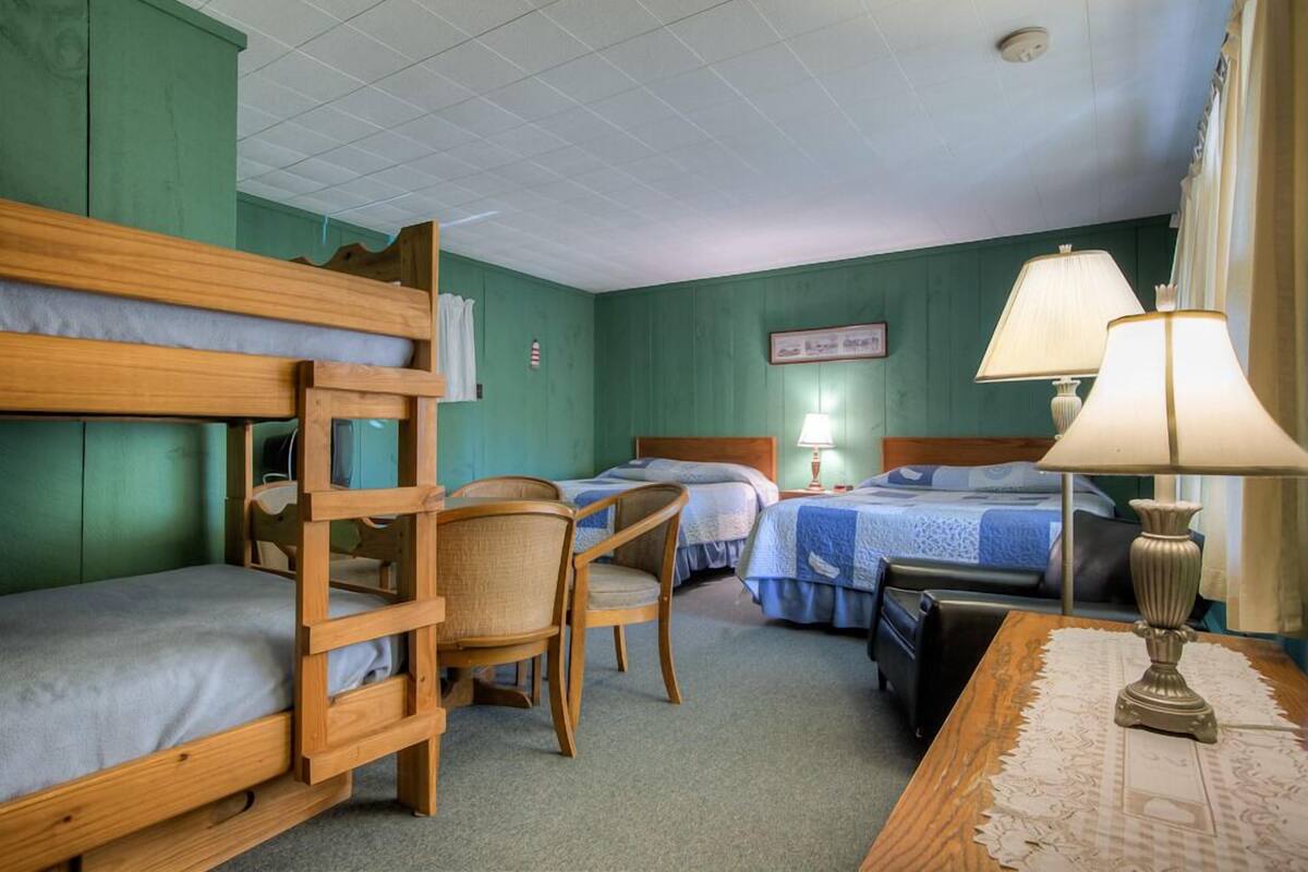 A room with bunk beds, a desk with a lamp, and a chair.