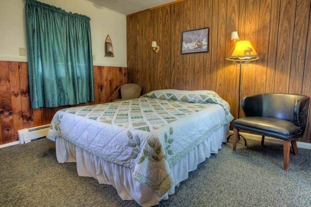 A room with a bed, a chair, a lamp, and a wall with wooden paneling.