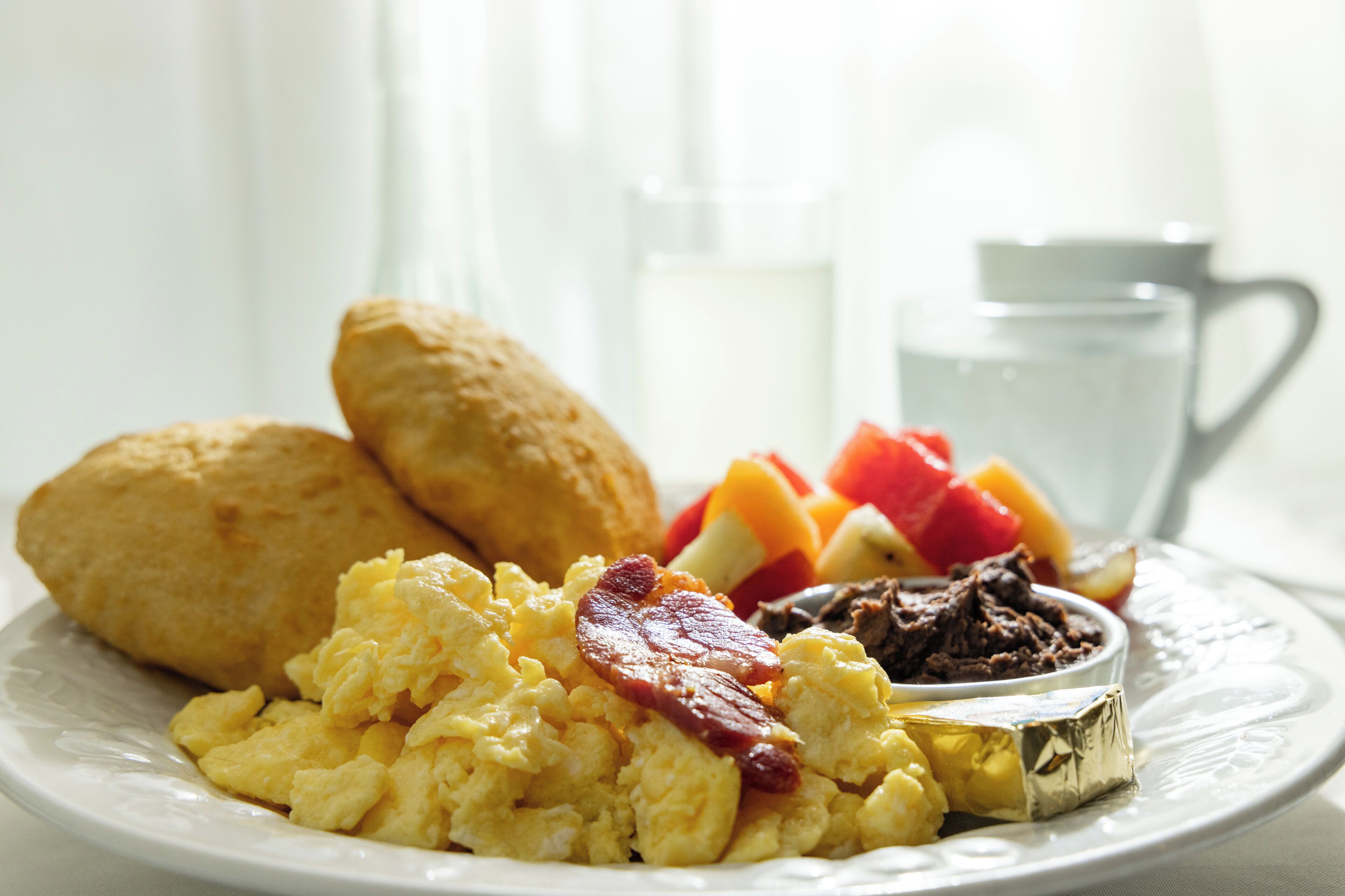 A plate of scrambled eggs, bacon, and a small bowl of chocolate spread.
