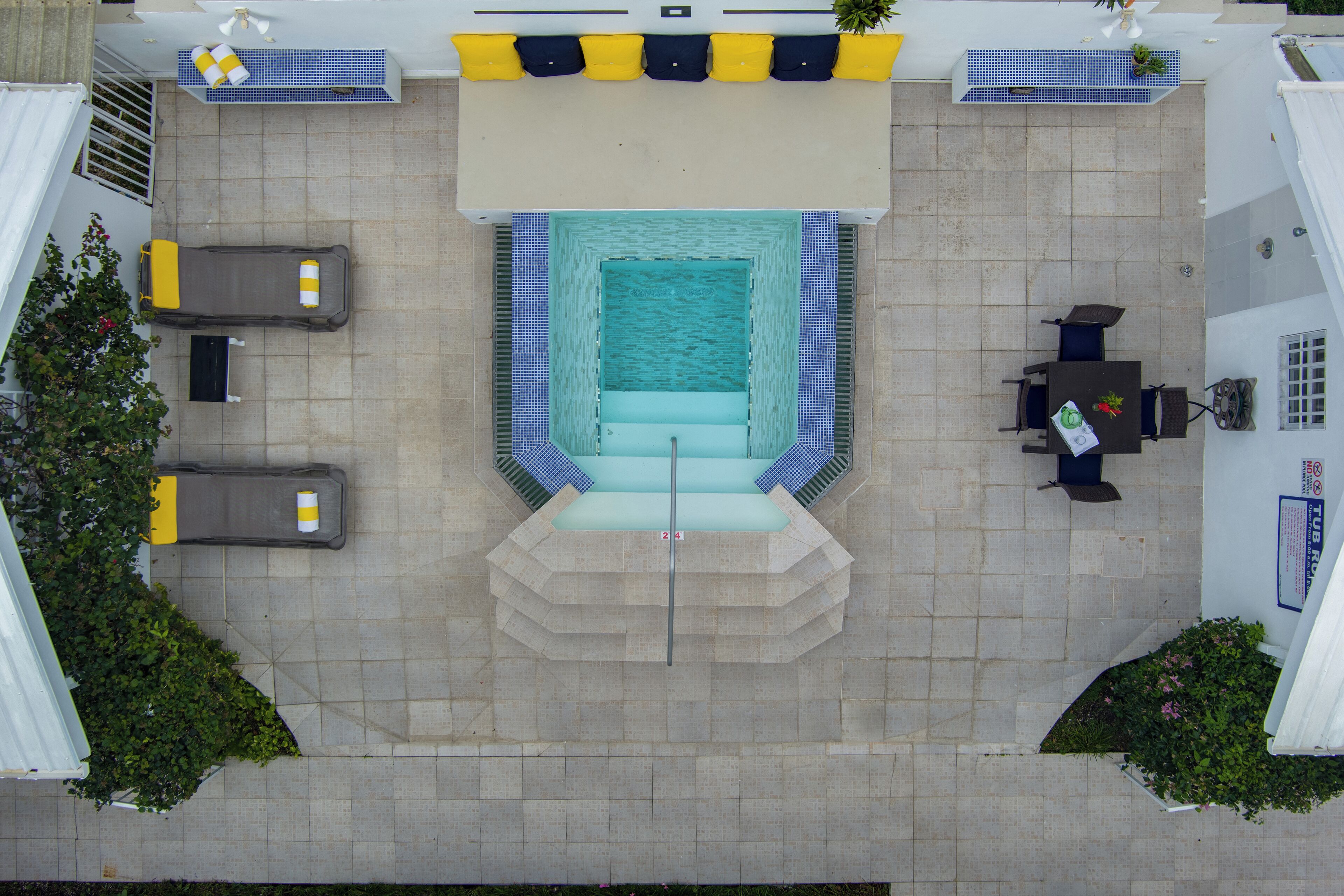 Vista aérea de una zona de piscina con una tumbona, una pequeña mesa con sillas y un banco.