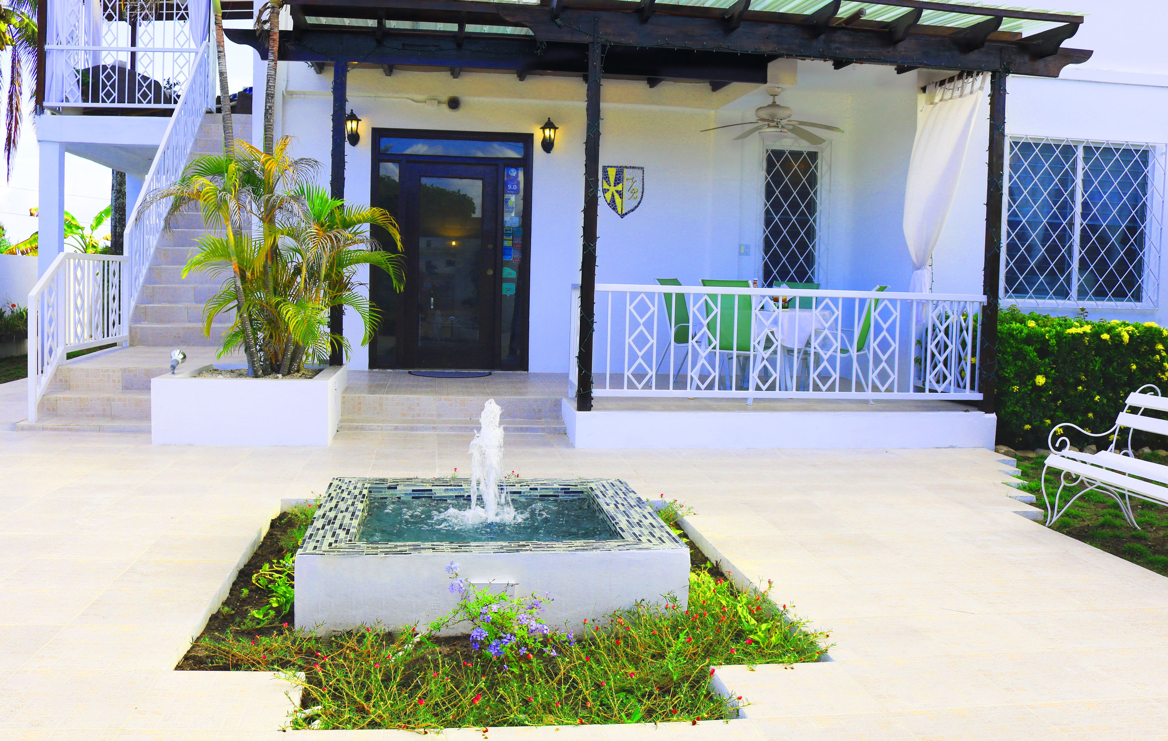 A courtyard with a fountain, a white bench, and a staircase leading to a balcony.