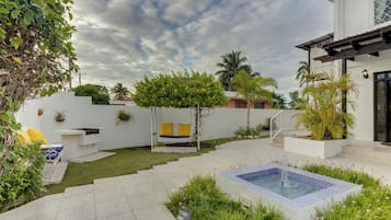 Un patio trasero con piscina, un muro blanco y un pequeño árbol.