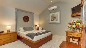 Un dormitorio con cama de madera, mesitas de noche, aire acondicionado, un cuadro enmarcado y un arreglo floral.