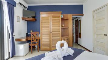 A hotel room with a bed, a desk, a chair, a wardrobe, and a bathroom visible through an open door.