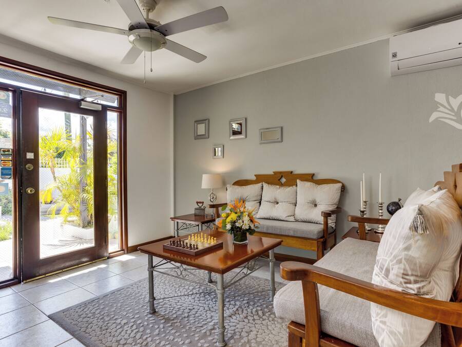 A living room with a sofa, a coffee table with a chessboard, a ceiling fan, and a door leading outside.