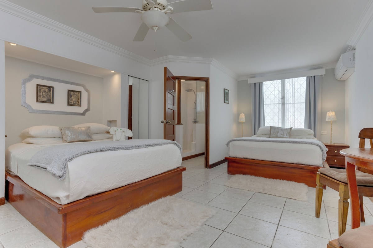 A bedroom with two beds, a ceiling fan, a wooden floor, and a white rug.