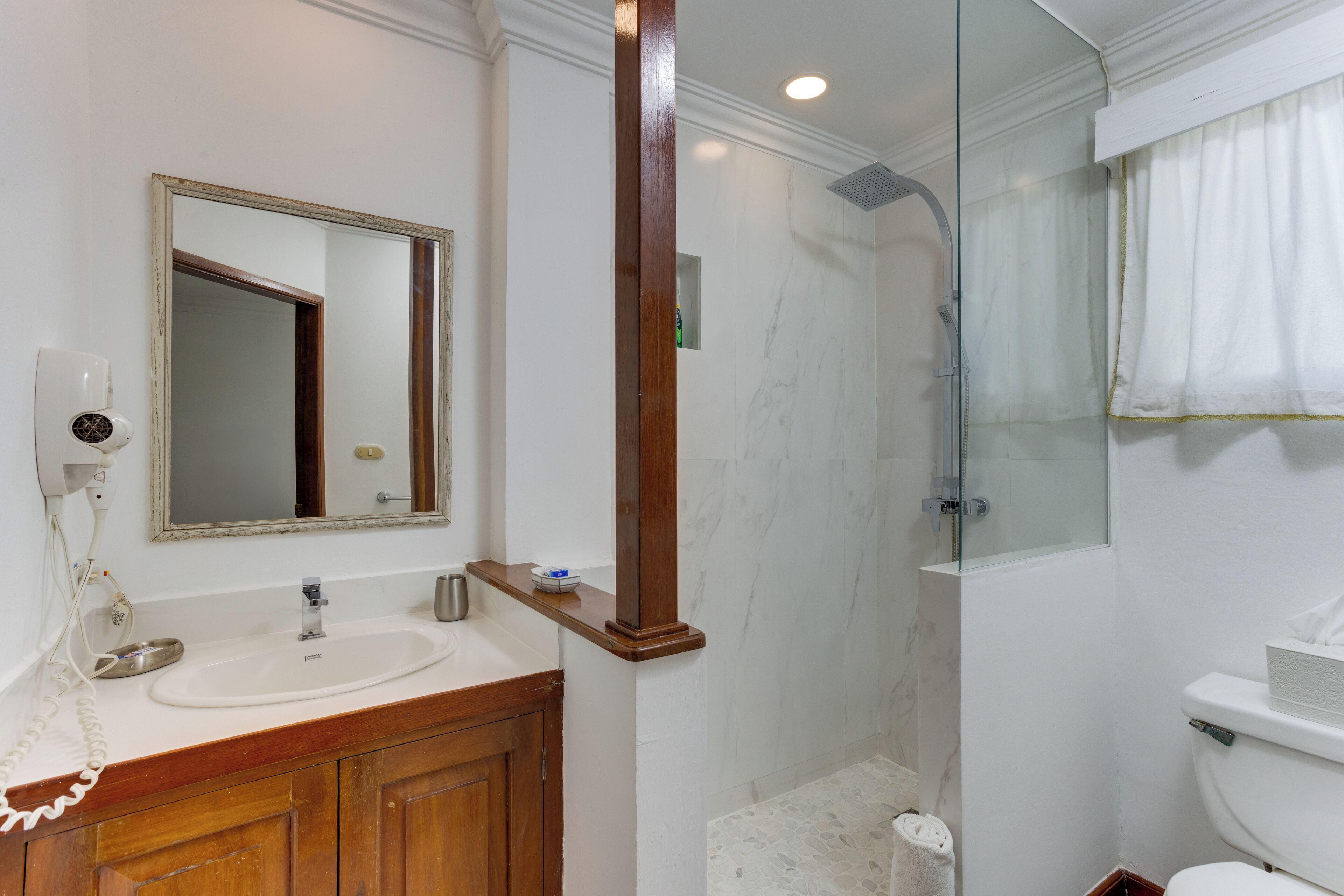 Un baño con tocador de madera, un espejo grande, cabina de ducha de vidrio y un inodoro.