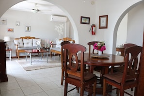 A dining area with wooden chairs and a round table, a sofa, and a coffee table with a vase of flowers. - Villa Boscardi (Belize City)