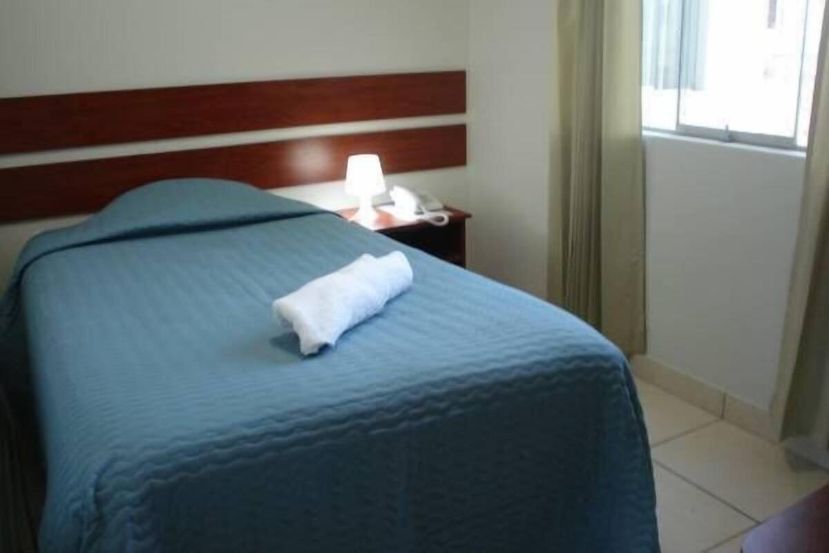 A hotel room with a bed, a nightstand with a lamp, and a window with curtains.