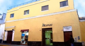 A yellow building with a sign for 'Herusalen' indicating it is a hotel. There is a visible entrance and a sign for 'Via Munde'. - Hotel Herusalen (Arequipa)