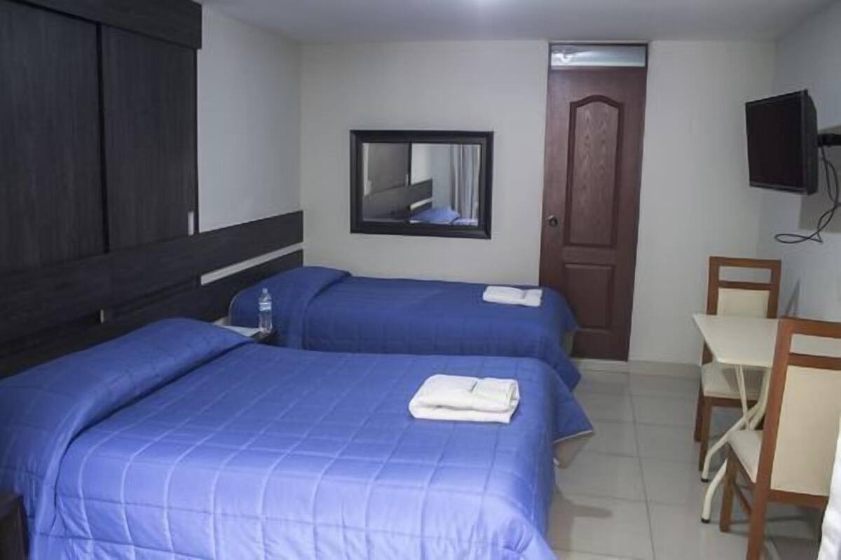 A hotel room with two beds, a desk, a chair, a television, and a door.